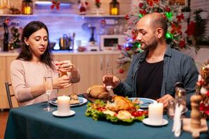 alegre romántico Pareja comiendo Navidad cena sentado a comedor mesa en Navidad decorado cocina. feliz familia disfrutando tiempo de Navidad celebrando invierno fiesta juntos foto