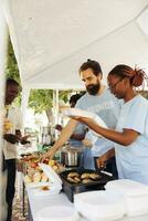 Young black woman and caucasian man cook and donate free meal at a food drive to the poor and needy. Charity workers helping homeless people, supporting hunger relief, and combating poverty. photo