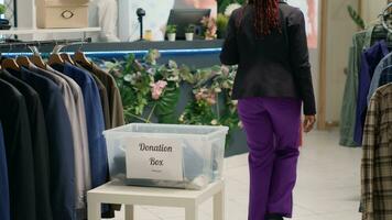 BIPOC shoppers in fancy fashion boutique donating their clothes for good cause. Customers placing garments in donation box, doing humanitarian gesture in premium clothing store photo