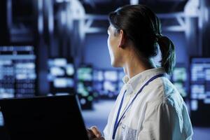 System administrator in data center uses laptop to prevent system overload during peak traffic periods. Overseeing manager in server farm ensuring enough network bandwidth for smooth operations photo