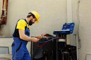 Capable serviceman hired to check external air conditioner freon tank in need of troubleshooting, using manometers. Qualified technician using manifold gauges looking at condenser refrigerant levels photo