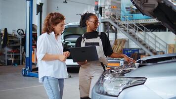 entrenado ingeniero en garaje utilizando ordenador portátil a seguir Lista de Verificación mientras haciendo mantenimiento en vehículo, hablando con cliente. trabajador en coche Servicio lo hace chequeo en automóvil siguiente a cliente foto