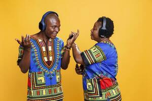 Cheerful black man and woman couple chatting while listening to music in wireless headphones. Mature boyfriend and girlfriend using mobile phone and talking while enjoying sound in earphones photo