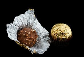 Unwrapped chocolate candy and wrapped in gold foil, on a black background. photo