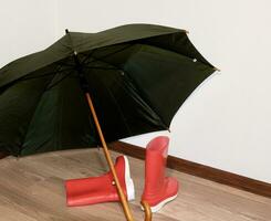 an open green umbrella lies on the floor and red rubber boots lie nearby photo