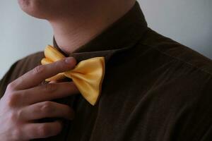In the photo a man's white hand is holding a golden bow tie