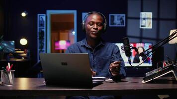 Portrait of BIPOC tech vlogger reviewing newly released smartphone in rgb lights living room studio. Entertaining influencer filming technology channel episode using professional video tools