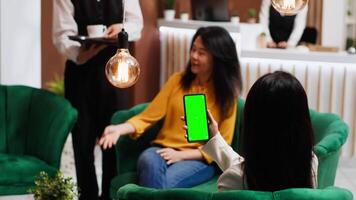 Customer looking at greenscreen layout on phone display, waiting for check in at hotel. Asian woman sitting on couch with smartphone showing blank copyspace mockup layout. Tripod shot. video