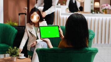 Hotel guest holding tablet with greenscreen layout in lobby, looking at chromakey isolated display and relaxing on sofa. Woman checking blank mockup copyspace screen on gadget. video