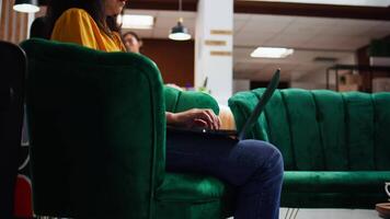 Hotel client solving issues on laptop in lounge area, waiting to register and see accommodation. Asian tourist passing time on pc, waiting to be called at front desk reception. Handheld shot. video