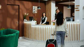 Tourist entering hotel reception to go through registration, confirming booking after long flight. Asian woman on holiday at five star resort, talking to front desk staff about room facilities. video