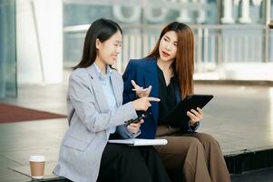 Businesswoman and woman going in city center in smart casual business style, talking, working together, stylish freelance people, holding tablet photo