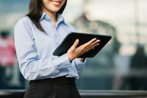 Young Asian business woman leader entrepreneur, professional manager holding digital tablet computer uon the street in big city photo