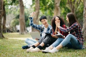 Three young college students is reading a book while relaxing sitting on grass in a campus park with her friends. Education concept photo