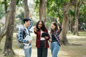 Three young college students is reading a book while relaxing sitting on grass in a campus park with her friends. Education concept photo