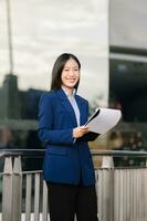 Young Asian business woman leader entrepreneur, professional manager holding digital tablet computer uon the street in big city photo