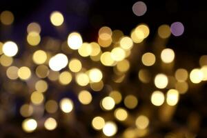 Yellow blurred bokeh lights of holiday decoration illumination in city. Abstract background with Christmas tree garland warm lights. Shiny defocused bokeh circles, dark blue backdrop. photo