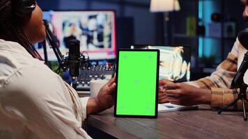 Green screen tablet hold by woman on podcast discussing with guest during marathon stream for humanitarian cause. Chroma key device used by host to check gathered donations from audience during show video