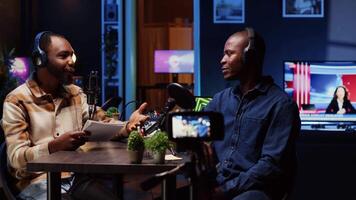 Internet show host making guest laugh, cracking jokes during comedy focused podcast. Talking show interviewer broadcasting live from living room studio decorated with neon lights video