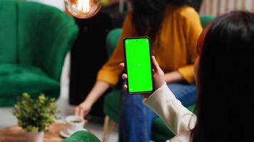 Woman checking greenscreen display on smartphone layout, passing time in lounge area at hotel. Asian tourist sitting on sofa with phone running isolated chromakey template on screen. video