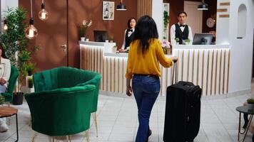 asiatisk kvinna närmar sig främre skrivbord i hotell lobby, receptionist be klient handla om rum bokning detaljer för kolla upp i. vänlig anställd välkomnande kund på reception, gästfrihet industri. video