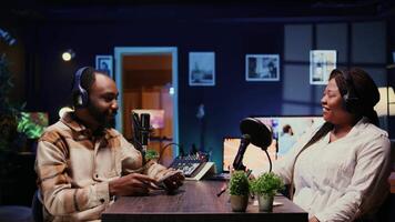 Vlogger show host interviewing guest in neon lights ornate studio, following questions written on paper. Man filming online podcast episode with woman, discussing about personal life video