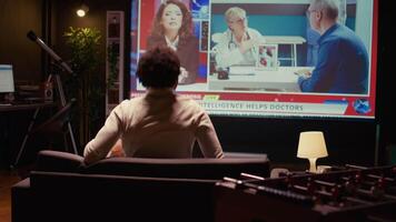 African american man watching news program on modern TV about artificial intelligence subject, zoom in close up shot. Cord cutter entertained by subscription service on ultrawide television screen video