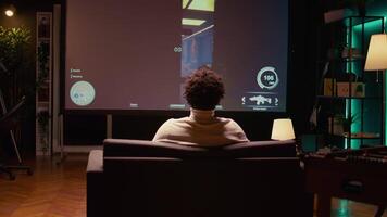 bipoc Mens spelen schutter videogame Aan ultrawide slim TV in futuristische industrieel instelling met Gezondheid, weerstand, munitie bars hud overlappen. zoom in schot van gamer genieten van pvp fps online multiplayer spel video