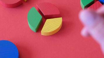 hands working with colorful wooden pie chart pieces on bright red background video