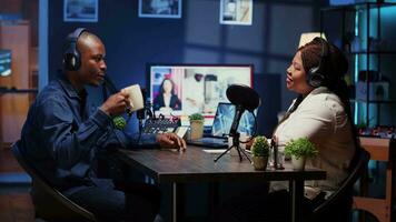 Show host recording podcast, enjoying cup of coffee and nice conversation with guest. African american man using professional audio devices for flawless sound quality while live chatting with woman video