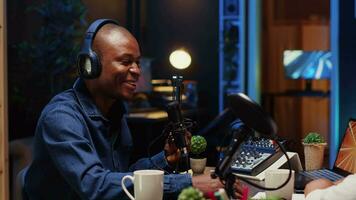 africano americano hombre grabación podcast, ajustando micrófono a garantizar óptimo sonido calidad para audiencia escuchando a hogar. contenido creador utilizando profesional audio productor dispositivos video