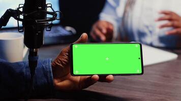 Close up shot of green screen phone hold by man invited to podcast watching internet clips in apartment studio. Chroma key smartphone running videos for podcasters to react to