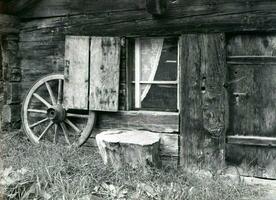 an old black and white photo of a wagon wheel and window