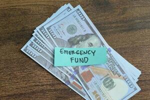 Concept of Emergency Fund write on sticky notes with Dollar isolated on Wooden Table. photo