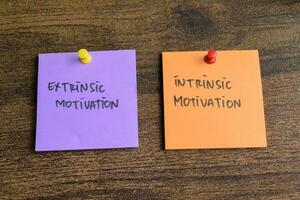 Concept of Extrinsic Motivation or Intrinsic Motivation write on sticky notes isolated on Wooden Table. photo