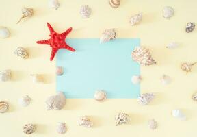 Trendy summer pattern made of sea shells and red starfish with light blue paper card note copy space on bright cream background. Minimal summer concept. Creative exotic summer flat lay. photo