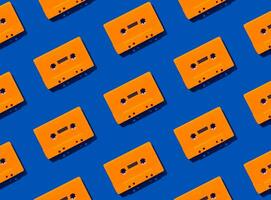 Pattern made with retro orange audio cassette tapes on blue background. Creative concept of retro technology. 80's aesthetic. Vintage audio cassette tape pattern idea. Retro nostalgia. Flat lay. photo