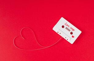Audio cassette with loose tape shaping a heart on red background. Minimal love concept. Creative retro technology love card. 80's aesthetic. Vintage cassette tape love songs idea. Retro nostalgia. photo