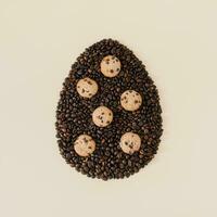 Creative composition with Easter egg shape made of roasted coffee beans and chocolate cookies on light cream background. Trendy Easter egg idea. Realistic aesthetic look. Flat lay. photo