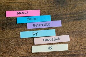 Concept of Grow Your Business by choosing us write on sticky notes isolated on Wooden Table. photo