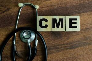 Concept of The wooden Cubes with the word CME with stethoscope on wooden background. photo