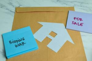 Concept of Bidding War and For Sale write on sticky notes isolated on Wooden Table. photo