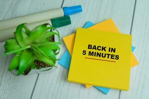 Concept of Back In 5 Minutes write on sticky notes isolated on Wooden Table. photo