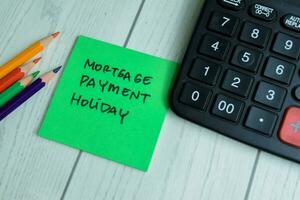 Concept of Mortgage Payment Holiday write on sticky notes with calculator isolated on Wooden Table. photo