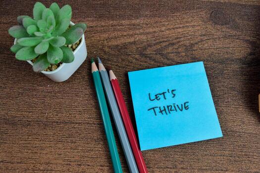 Concept of Let's Thrive write on sticky notes isolated on Wooden Table. photo