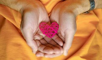 Hand-made raspberry heart in male hands on an orange background photo