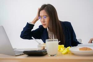 mujer de negocios ocupada y cansada comiendo espagueti para el almuerzo en la oficina y trabajando para entregar estados financieros a un jefe. con exceso de trabajo y poco saludable para comidas preparadas, concepto de agotamiento. foto