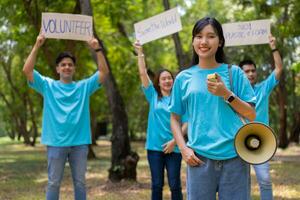 Happy young Asian students diverse volunteers hold a campaign sign for cleaning in the park, The concept of environmental conservation on world environment day, recycling, charity for sustainability. photo