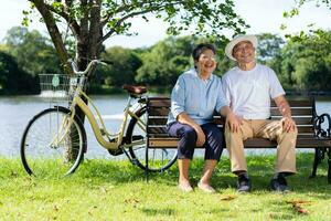 Happy and healthy couple Asian sitting chair beside a bicycle Family and friendship lifestyle, Enjoyment of active seniors, and outdoor activity after retirement, health care insurance concept photo