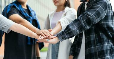 Group of cheerful young Asian entrepreneurs joining hands together to celebrate, excited success for achievements obtained. Undergraduate students celebrate success after end project, teamwork concept photo